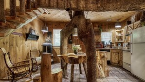 A rustic cabin interior with a wooden dining table surrounded by tree stumps, a rocking chair, and a kitchen area with a refrigerator and microwave. - ER69 - Rachel's Tree House - Great location. Close to all the action! (Pigeon Forge)