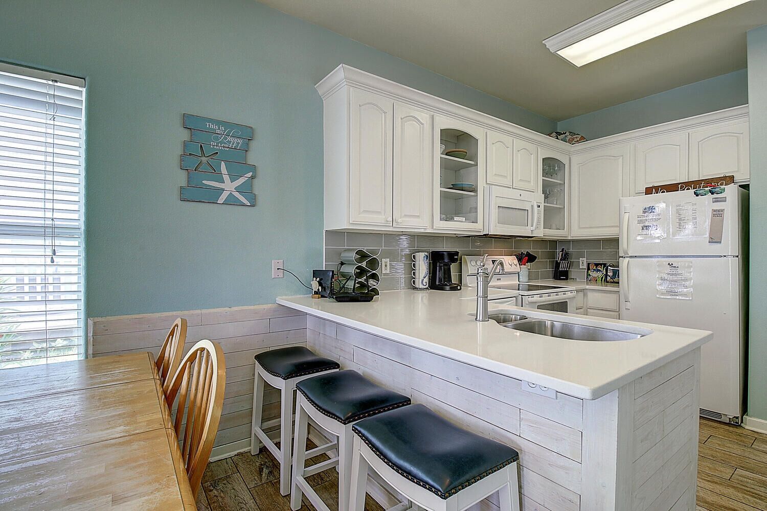 A kitchen with white cabinets, a bar area with stools, a coffee maker, and a refrigerator.
