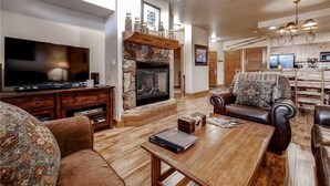 Ein Wohnzimmer mit Kamin aus Stein, einem Fernseher, Ledersofas und einem Holztisch.