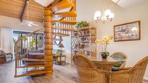Een ruime woonkamer met een houten spiraaltrap, rieten meubels en een boekenplank.