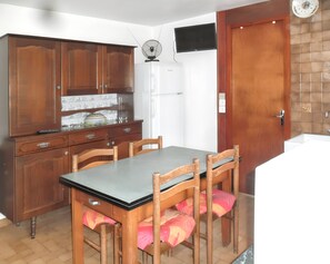 Una cocina con armarios de madera, un refrigerador, una mesa de comedor con sillas y un reloj en la pared.