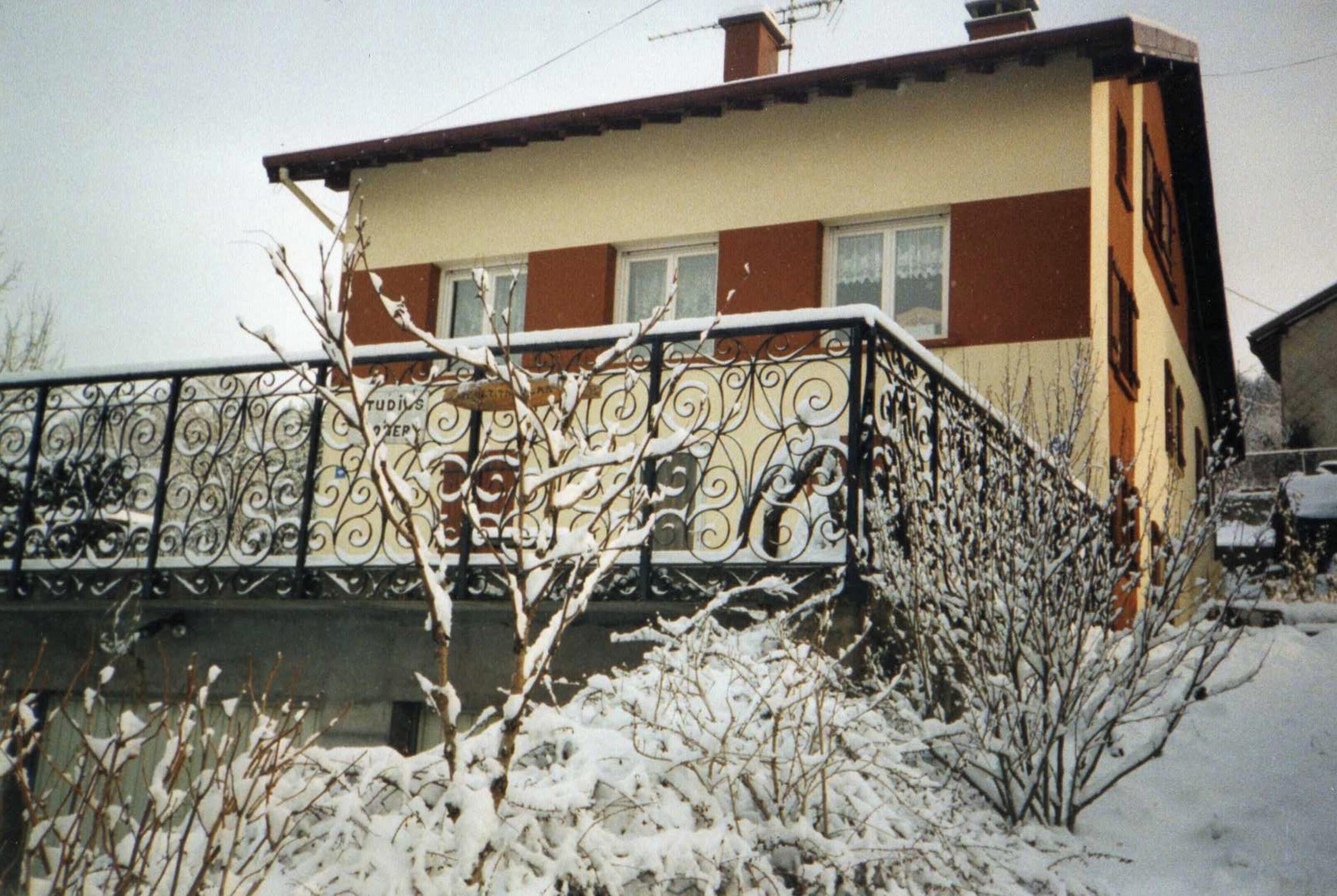 Ein Haus mit einem Balkon, einem Schild mit Schriftzug und schneebedeckten Pflanzen.