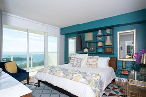 A bedroom with a large bed, a view of the ocean, and a balcony.
