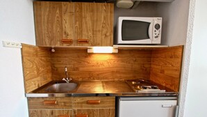 A compact kitchenette with wooden cabinetry, a stainless steel sink, a microwave, and a small refrigerator.