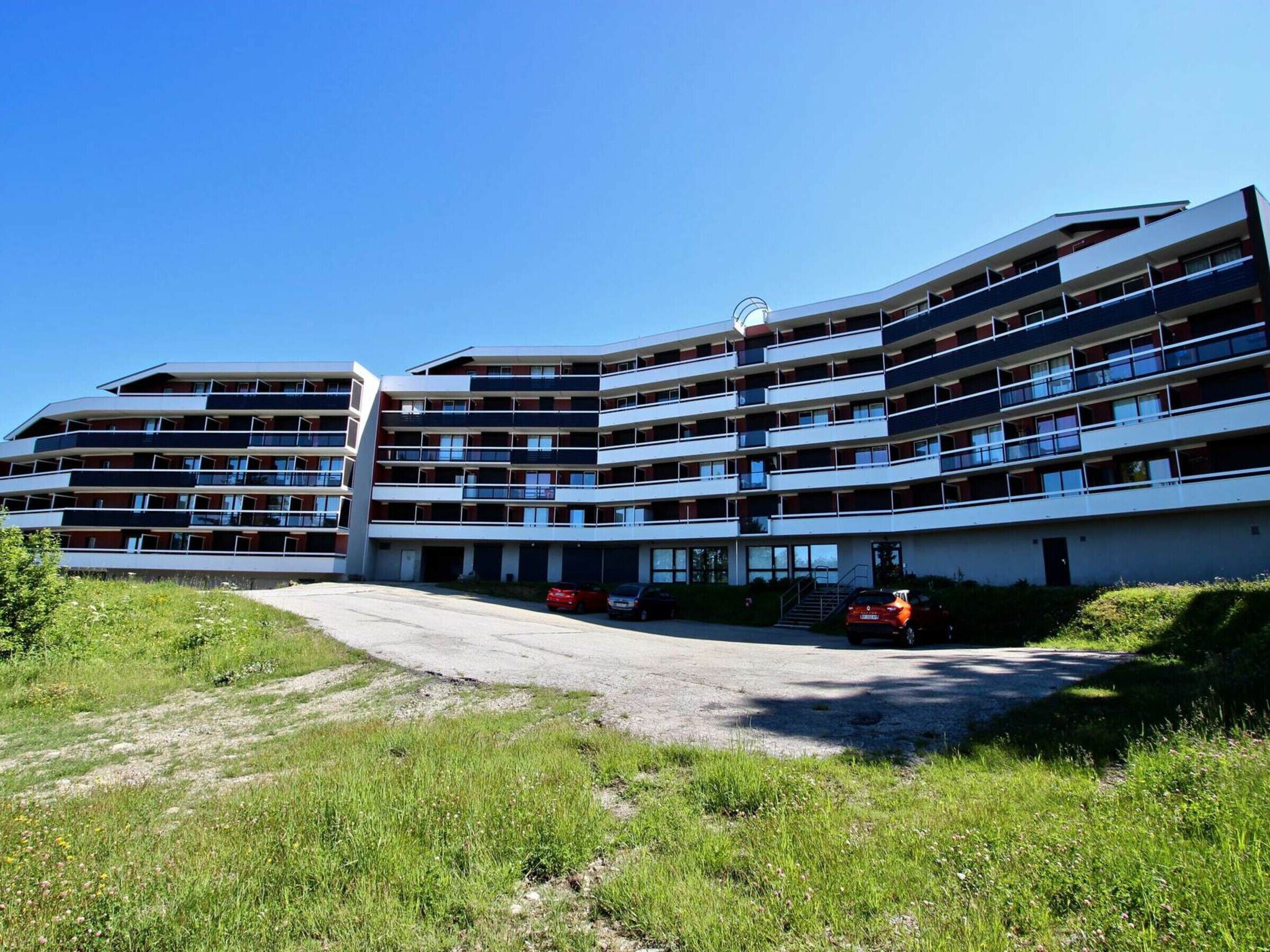 Un hotel de varios pisos con fachada curva, múltiples balcones y una zona de estacionamiento.