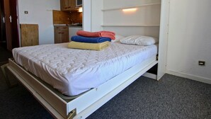 A single bed with a white mattress and quilt, a wooden headboard, and a small bedside table.