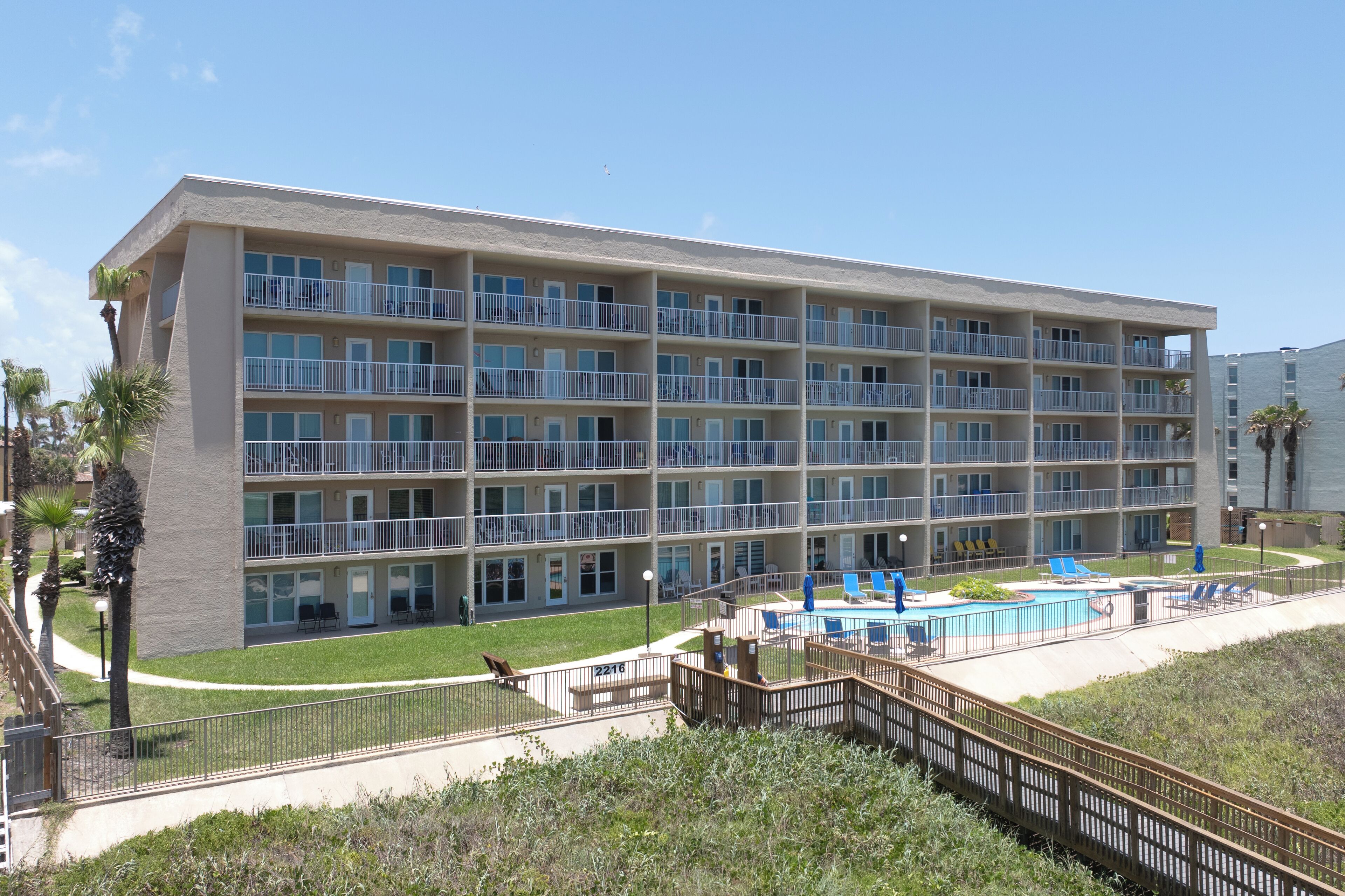 A multi-story hotel with balconies, a swimming pool, and a grassy area.