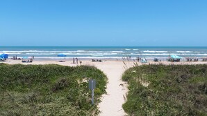 A beach path leading to the ocean with umbrellas and beach chairs.