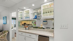 A modern kitchen with white cabinets, glass shelves, and a granite countertop.