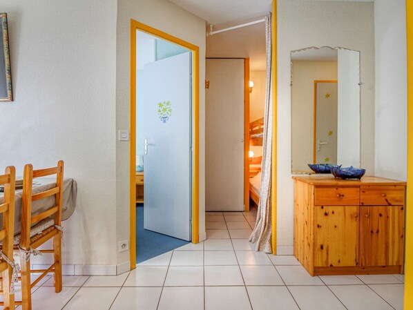 A room with a wooden dining table and chairs, a wooden cabinet with blue bowls, and a door leading to another room with a bunk bed.