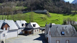 A cluster of houses with sloped roofs, a stone wall, and a green hillside in the background. - T2 cabin 6 people in Luz, quiet, parking, pets allowed (Luz-Saint-Sauveur)