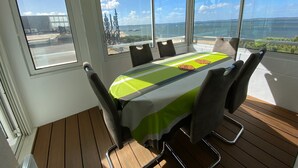 Un salón de conferencias con una mesa, sillas y ventanas amplias que dan a vista al mar y un puente.