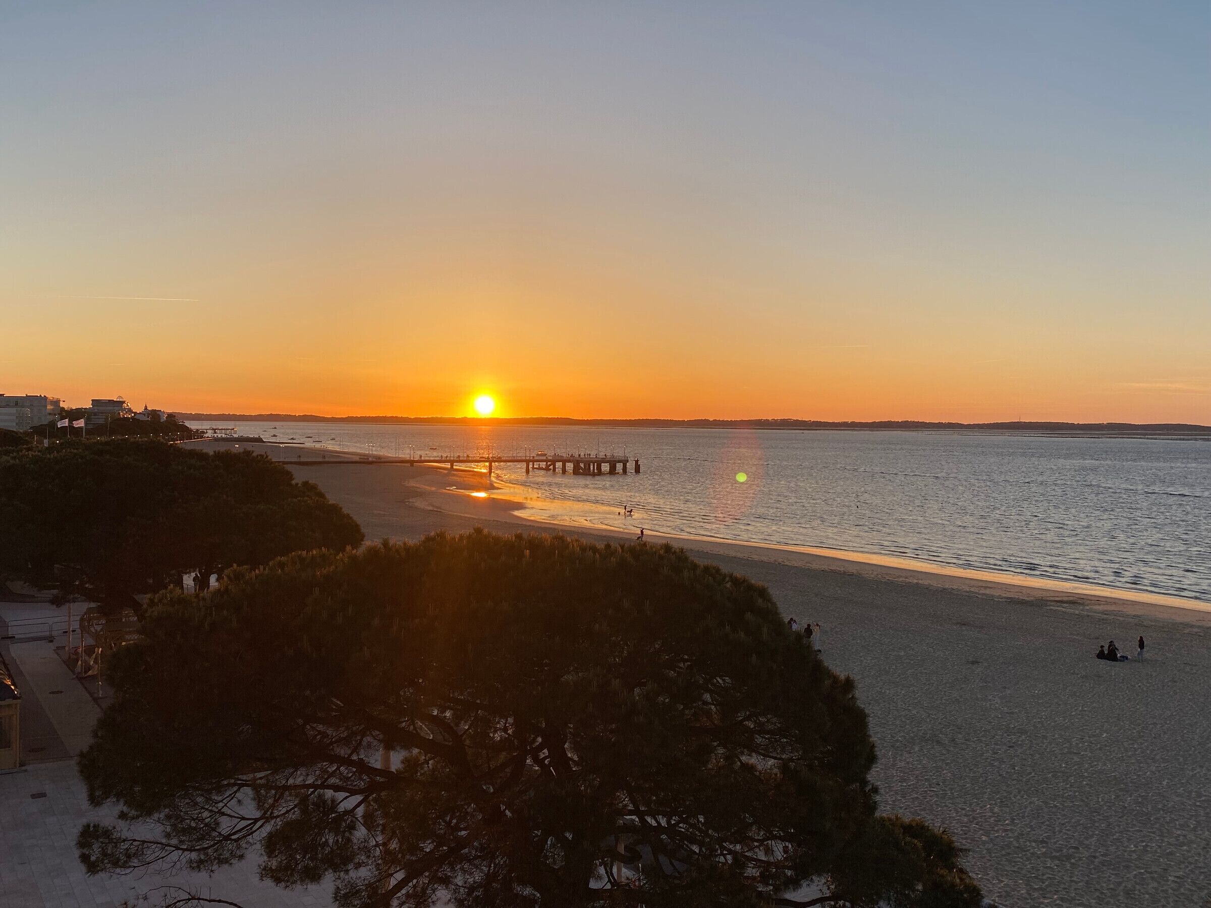 A sunset over a beach with a pier extending into the water.