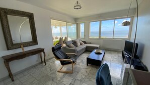 Amplia sala de estar con un ventanal que ofrece vista al mar, un sofá cómodo, un sillón de cuero negro, una mesa de centro y un televisor.