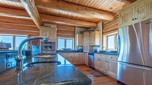 A spacious kitchen with wooden beams, a stainless steel refrigerator, and a large island with a sink. - Teton Homestead: Teton Summit View Log Home (Driggs)