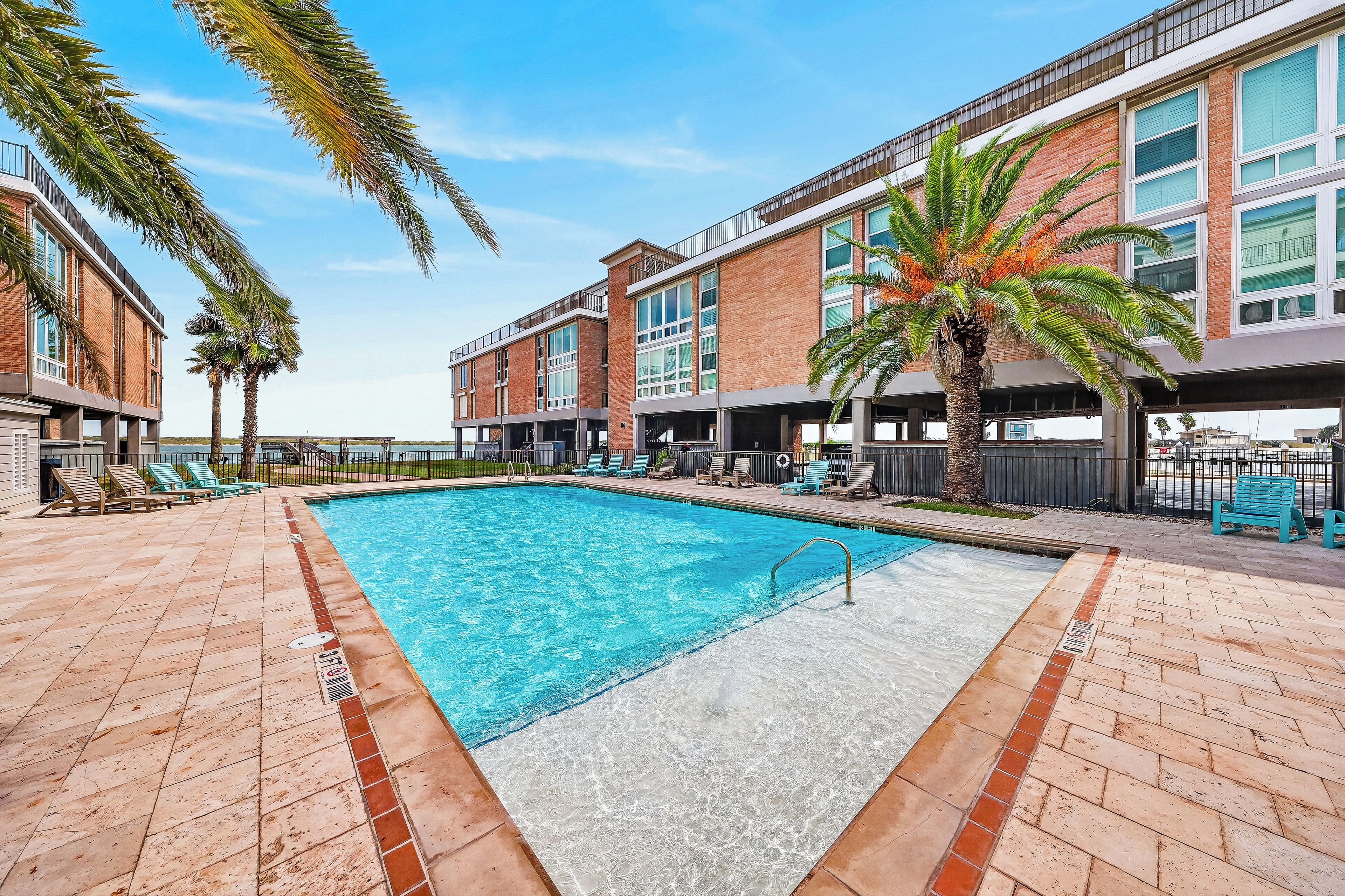 A swimming pool with a clear blue water surface, surrounded by a brick deck with lounge chairs.