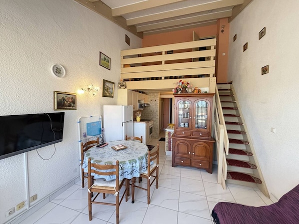 Un espace de vie compact comprenant un coin repas, un téléviseur, un escalier et un meuble de rangement.