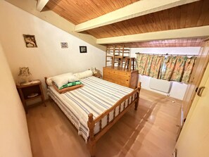 Une chambre à coucher avec un lit en bois, une table de chevet, une commode et une fenêtre avec des rideaux.