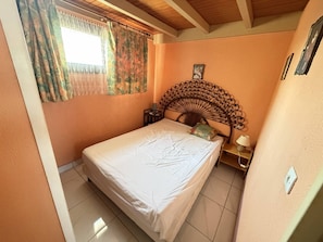 Quarto com cama, mesa de cabeceira, quadro na parede e janela com cortinas.