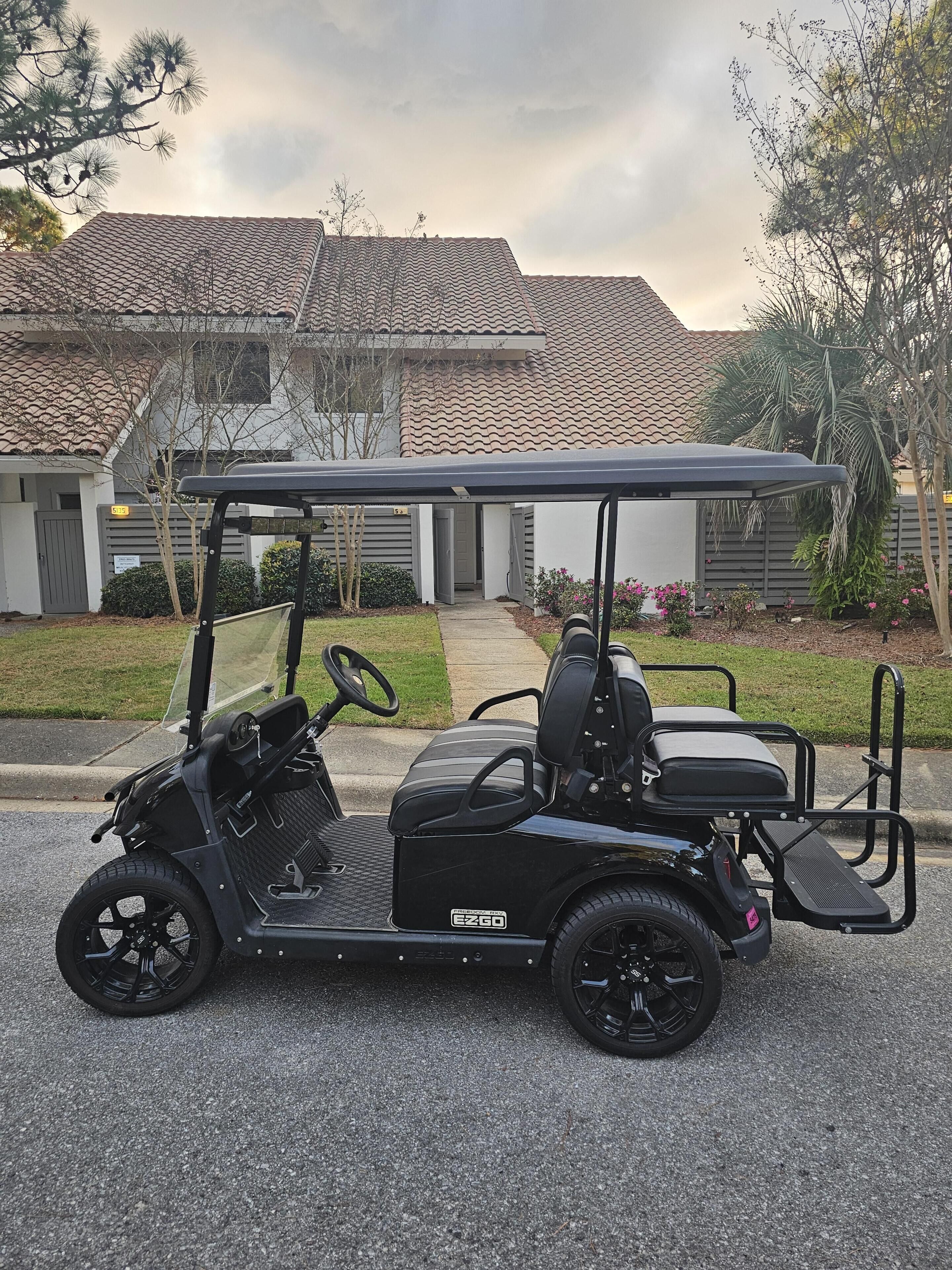 A black golf cart parked in front of a residential house with a tiled roof.