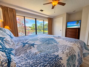 A bedroom with a large bed, a ceiling fan, a television, and a view of a lake. - Beachside of Sandestin Resort. Close to pool | Golf Cart Included. New Flooring thoughout! (Destin)