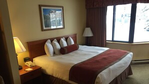 Een hotelkamer met een groot bed, een nachtkastje met een lamp, een telefoon en een ingelijst schilderij aan de muur.