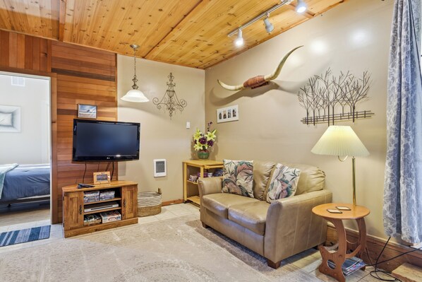 Un salon chaleureux avec un plafond en bois, un canapé en cuir, un téléviseur posé sur un meuble en bois, une lampe et un élément de décoration fixé au mur.