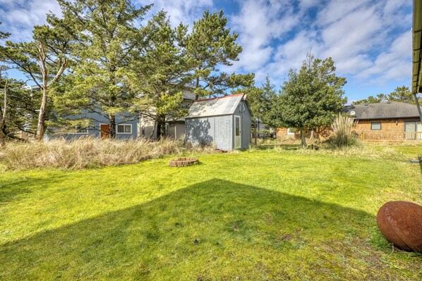 A grassy yard with a small shed, a wooden house, and trees.