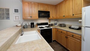 A kitchen with wooden cabinets, a microwave, stove, sink, and a refrigerator. - 227D: Large Two Story Home, 1 Block from the Beach, Fireplace, Hillside Views - (Avalon)