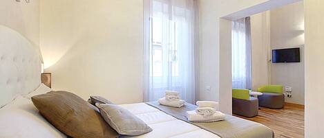 A hotel room with a large bed, a TV, and a seating area with chairs.