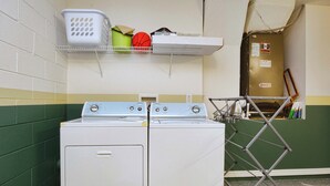 Un área de lavandería con lavadora y secadora, un tendedero y un estante con una cesta y una pelota de baloncesto.