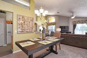 A dining area with a table set for four, a chandelier, and a large painting on the wall. - Family-Friendly Disney Retreat | Private Pool, Game Room & Lake View-2201EM (Kissimmee)
