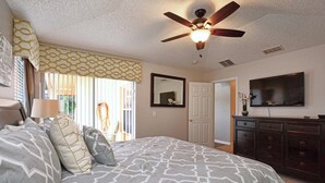 Un dormitorio con cama, ventilador de techo, cómoda, televisor y puerta.