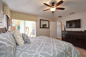 A bedroom with a bed, a ceiling fan, a dresser, a television, and a door. - Family-Friendly Disney Retreat | Private Pool, Game Room & Lake View-2201EM (Kissimmee)