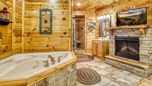 A log cabin interior with a stone fireplace, a large bathtub, and wooden walls. - Declan's View - Cozy 1 bedroom with Game room and Great Mountain Views! (Sevierville)