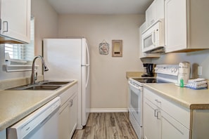 A compact kitchen with white appliances, a sink, and a countertop. - Beautiful Gulf Views at Sea Isle Village! (Port Aransas)