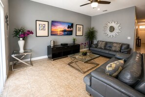 A living room with a sofa, coffee table, TV, and decorative items. - Private Pool & Spa | No Rear Neighbors | Walk to Clubhouse | 6BR Near Disney (Kissimmee)