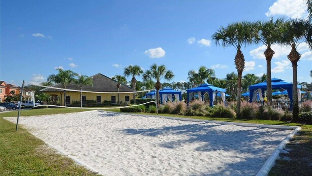 Een zandvolleybalveld met blauwe parasols en palmbomen.
