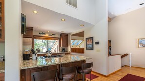 A kitchen with a large island, bar stools, wooden cabinets, and a view of the outdoors. - CHER06 - Great for Groups, A/C, Hot Tub (Sunriver)