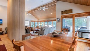 A spacious living area with a wooden dining table, a sofa, and a large window offering a view of the outdoors. - CHER06 - Great for Groups, A/C, Hot Tub (Sunriver)