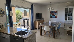 Uma cozinha moderna com forno embutido, um espaço de jantar com mesa e cadeiras, uma TV e um quadro na parede.