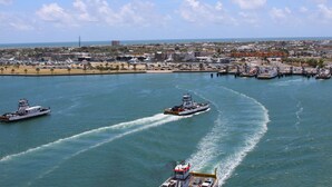 Un port de plaisance où plusieurs bateaux sont amarrés et un grand navire se déplace sur l’eau.