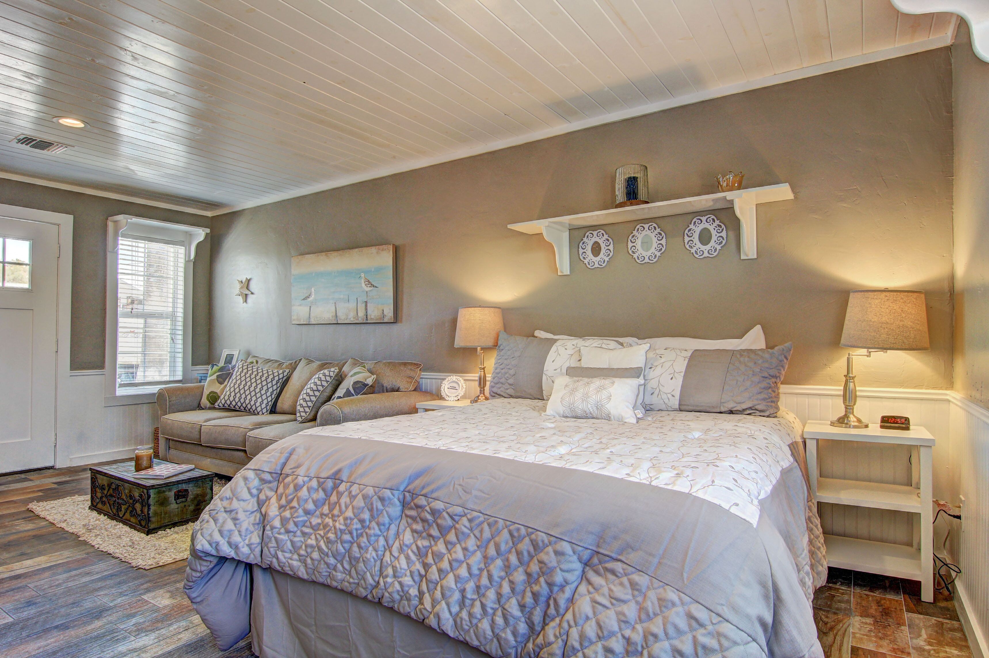 A bedroom with a large bed, a nightstand, a dresser, and a window with blinds.