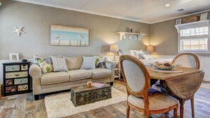 Un salon chaleureux avec un canapé beige, une table à manger en bois et une décoration en forme d’étoile de mer accrochée au mur.