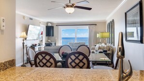 A dining area with a table and chairs, a ceiling fan, and a view of the ocean through large windows. - 🌊 Islander #609 – Coastal Elegance with Stunning Gulf Views! 🏖️✨ (Destin)