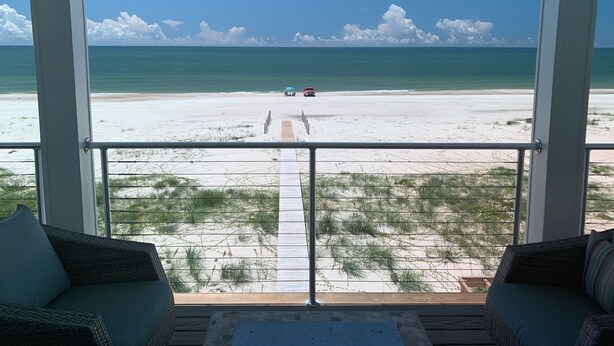 A beach view from a balcony with a wooden deck, two wicker sofas, and a clear sky.