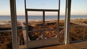 A room with a large window overlooking a beach with a wooden deck and a boardwalk.