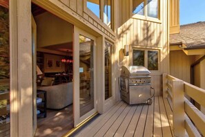 A wooden deck with a grill, sliding glass doors to a living area, and a view of the outdoors.