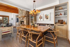 A dining area with a wooden table and chairs, a stone fireplace, and a chandelier.