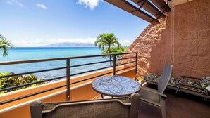 A balcony with a view of the ocean, a round table, and two chairs.